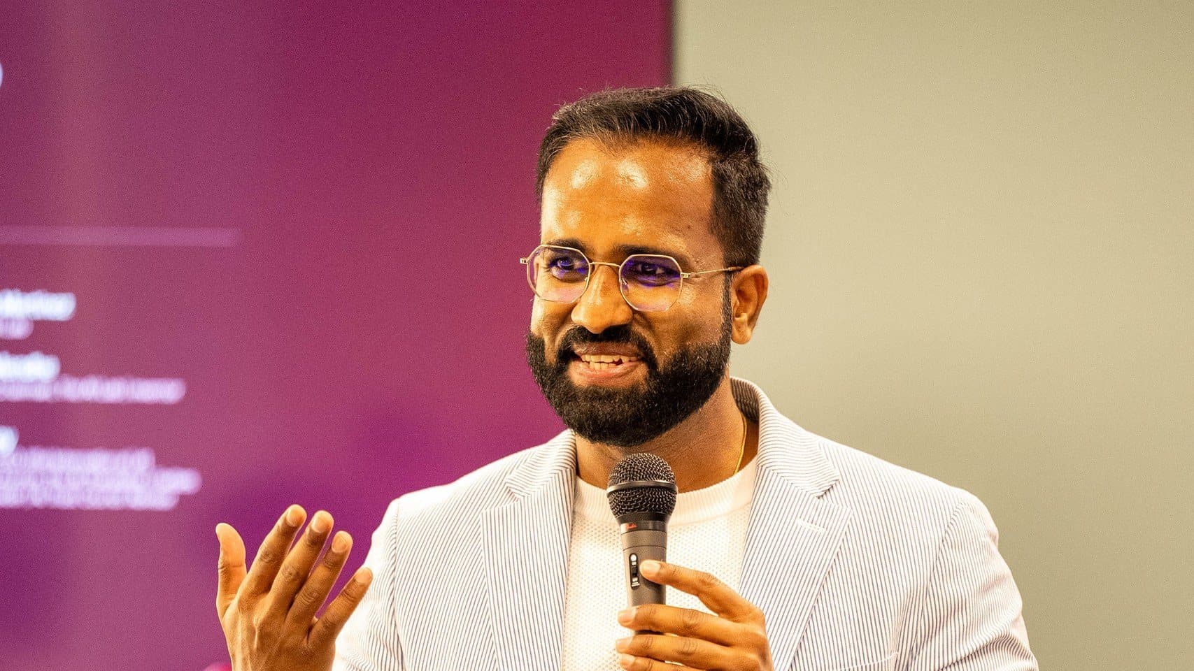 Dinesh Mendhe, Founder and Chairman of The AI Lab, speaks into a microphone in front of a purple OC Tech Week presentation screen.