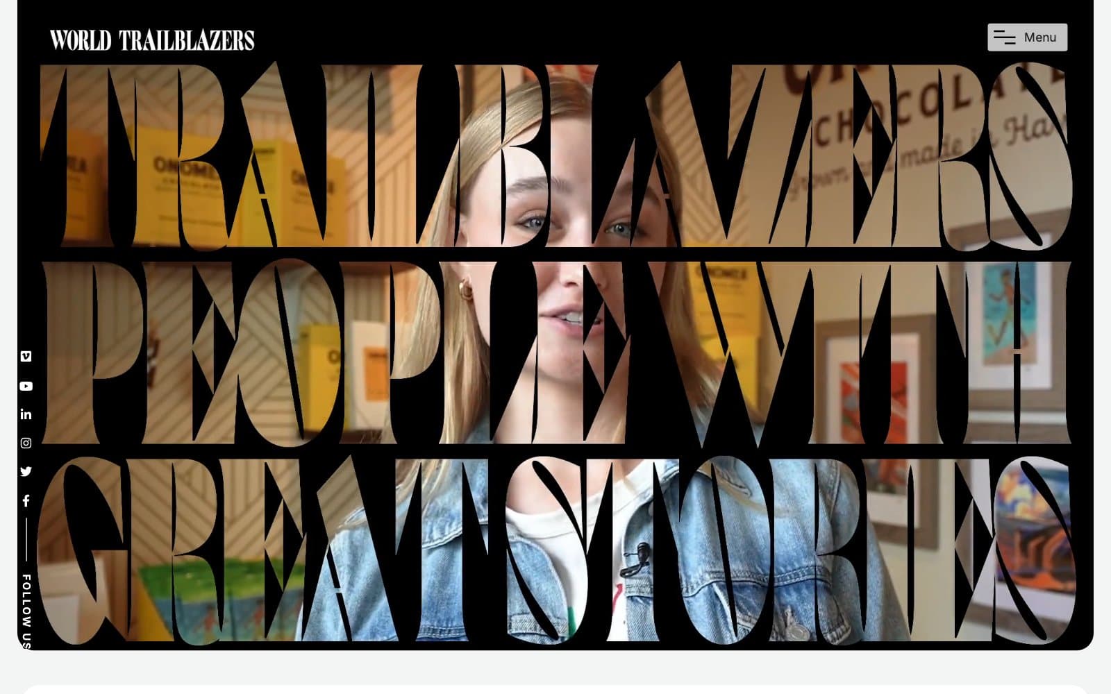 The World Trailblazers homepage, with the words Trailblazers, People With Great Stories cut out of a black screen in tall serif letters over video of a smiling woman in a shop